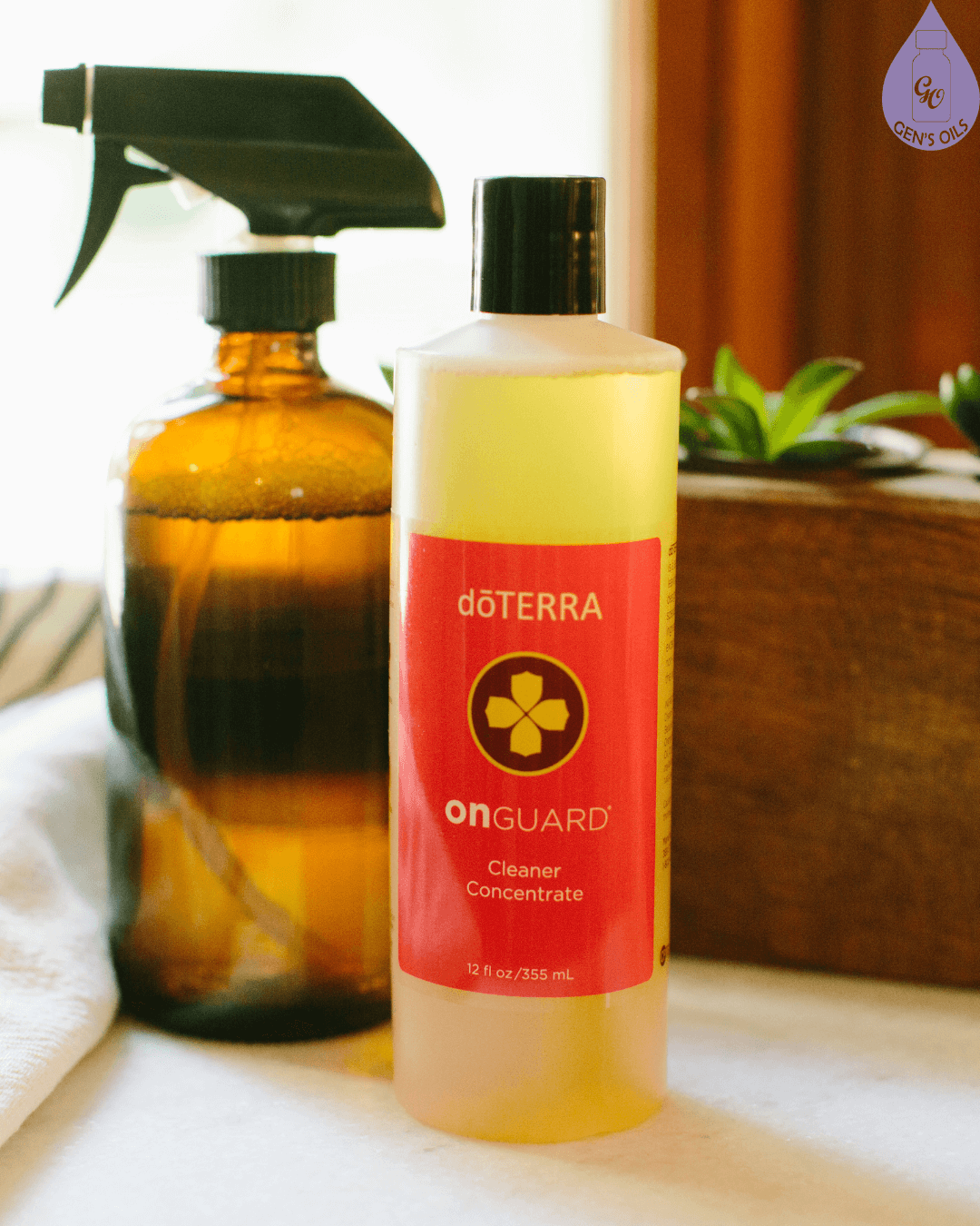 A bottle of DoTERRA OnGuard cleaner concentrate sits next to a brown glass spray bottle and a wooden planter with succulents.