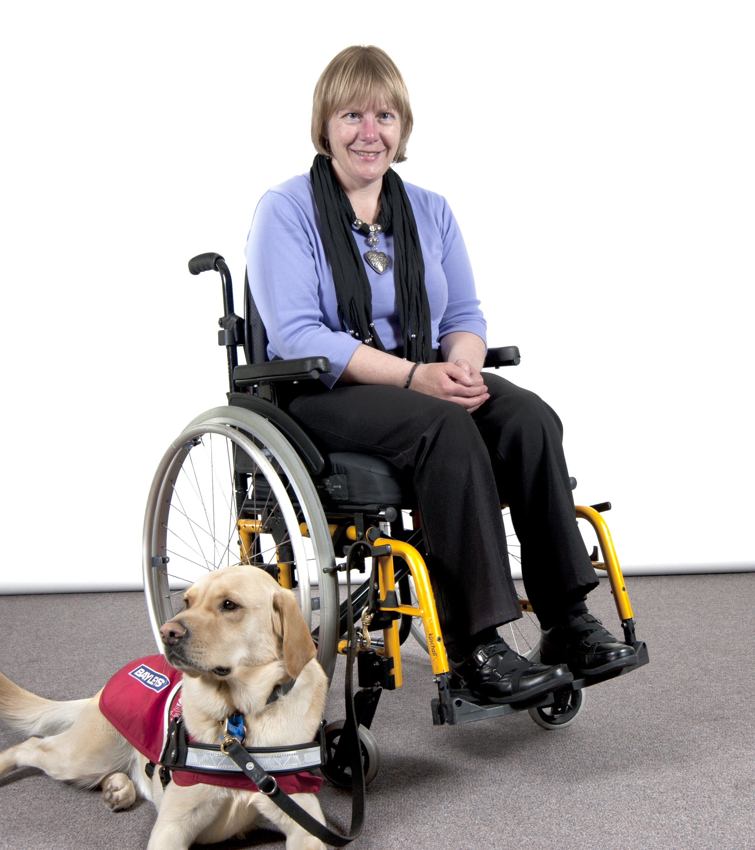 Genevieve sitting in her wheelchair with Guide Dog Pedro lying beside her.