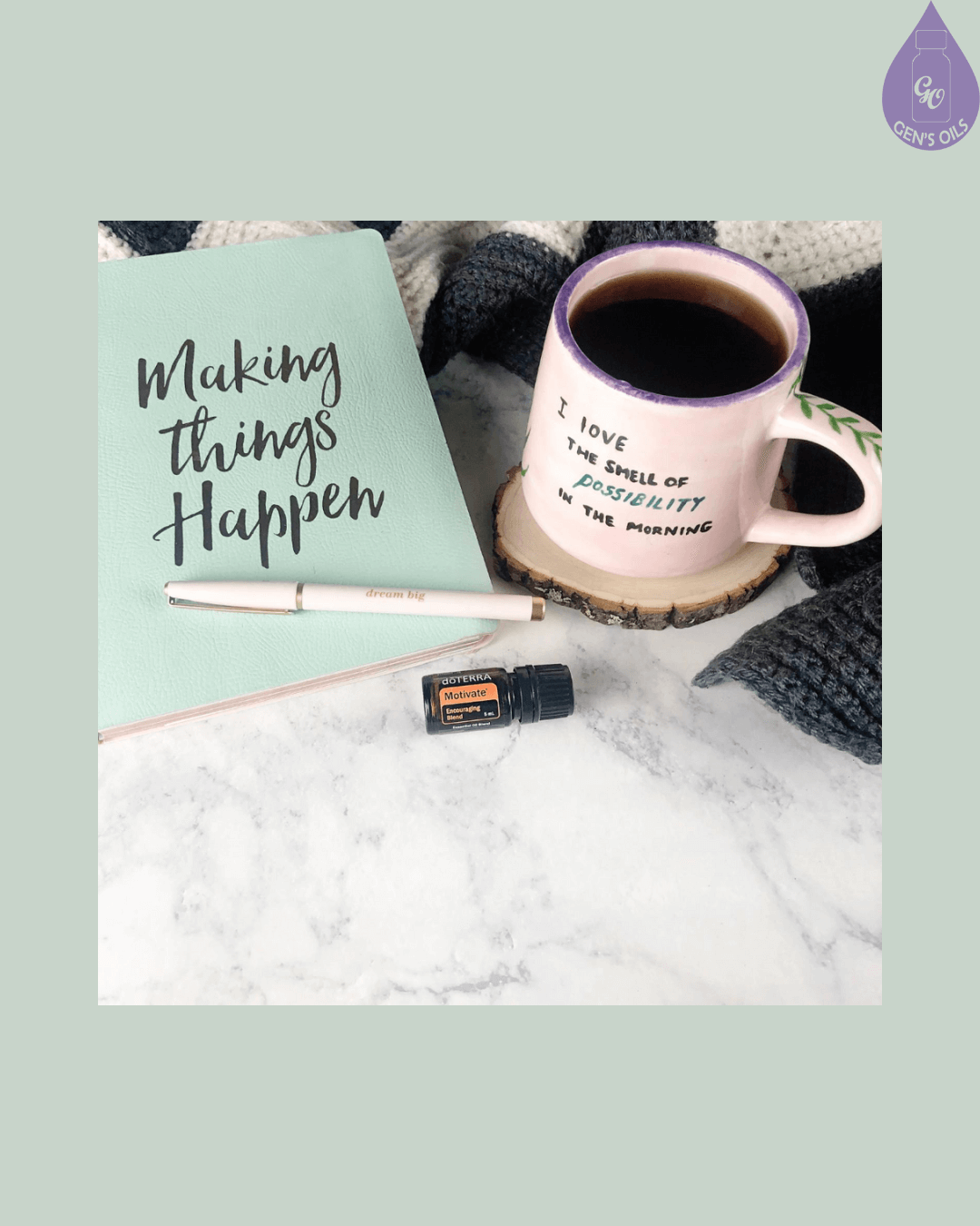 A mint green notebook with the words "Making things Happen" written on it, a pink pen, a mug of coffee that says "I love the smell of possibility in the morning", and a small bottle of essential oil on a marble surface.