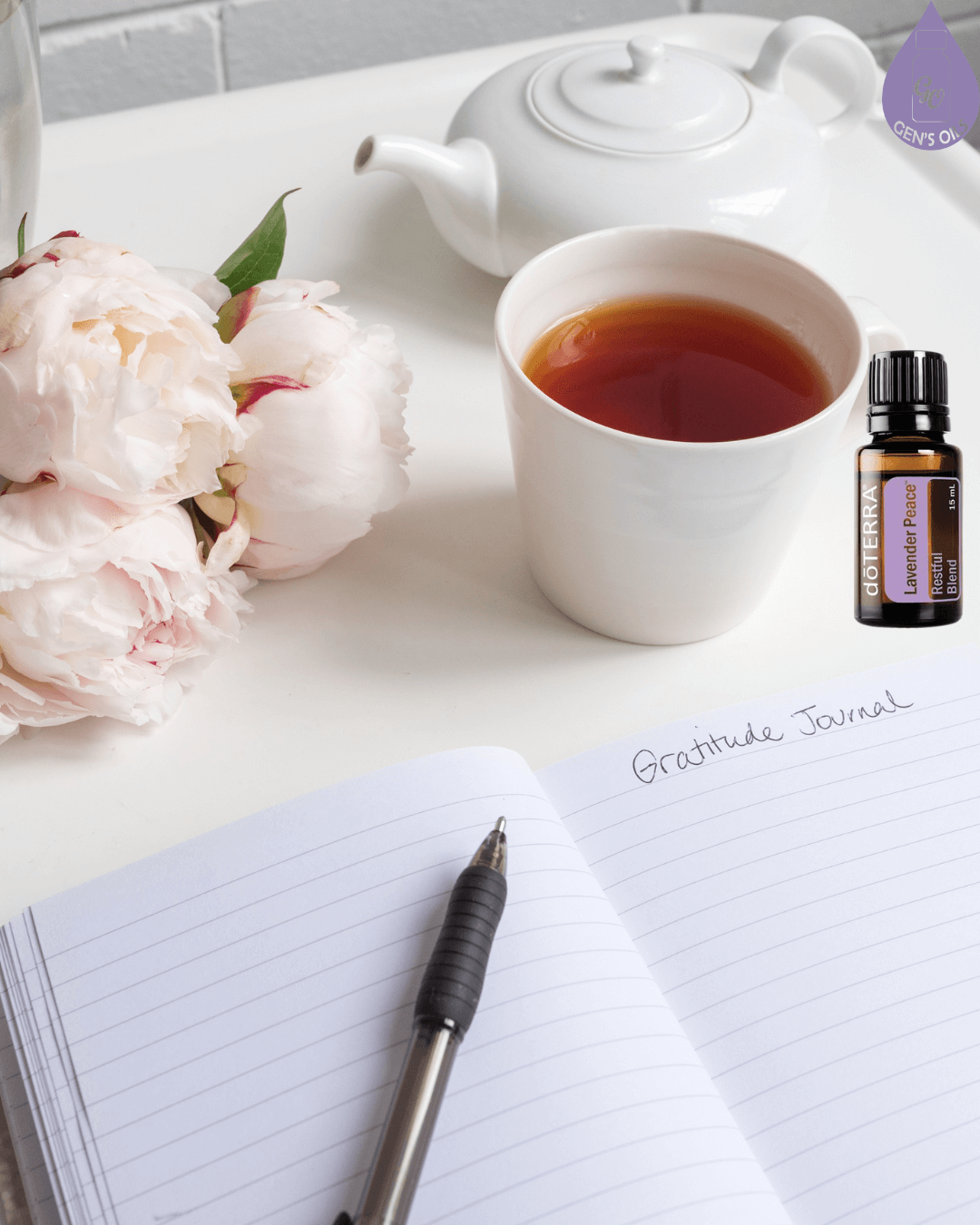A journal with 'Gratitude Journal' written on the page, a cup of tea, a teapot, a vase with flowers & a bottle of Lavender Peace essential oil on a tray.