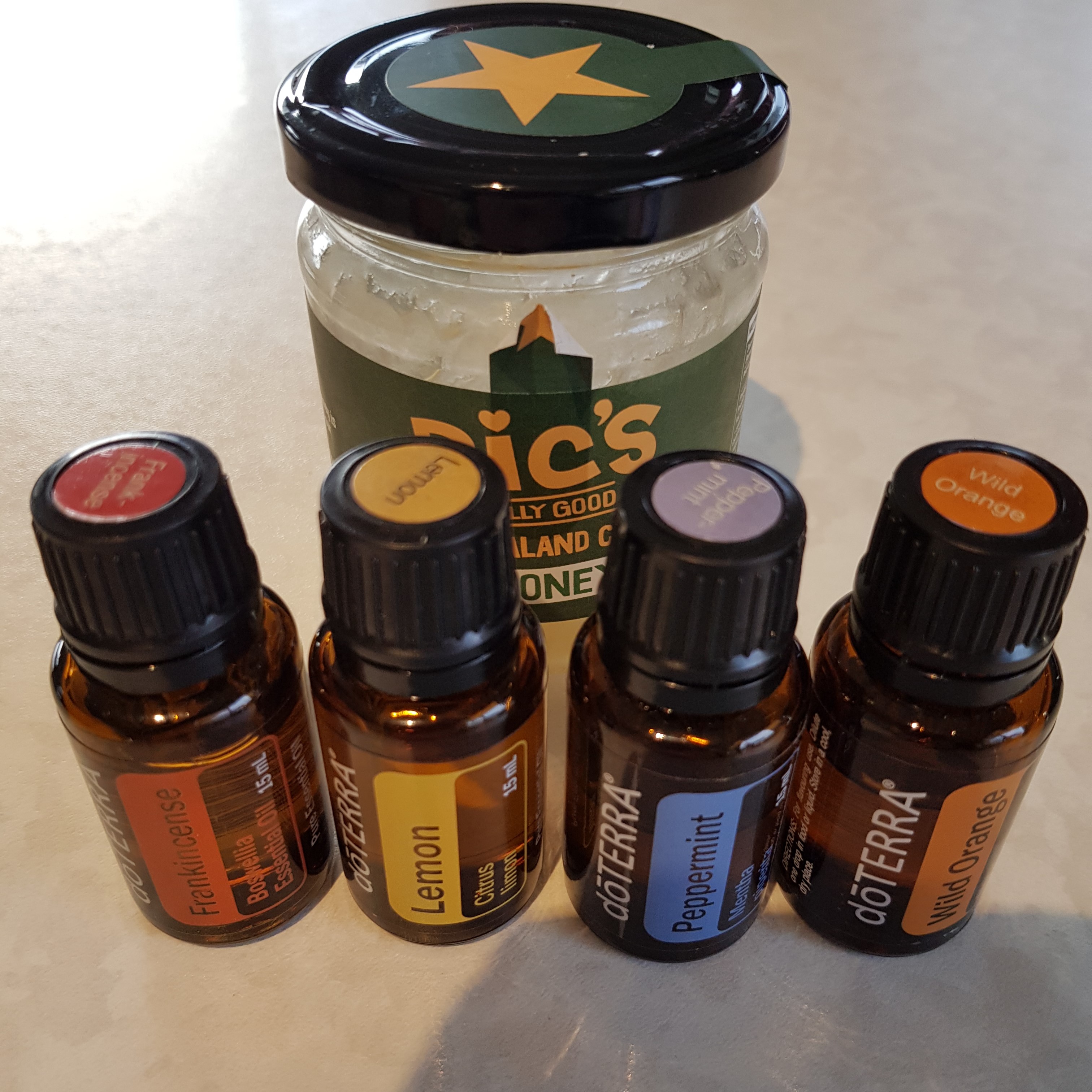 A jar of honey in the background with Frankincense, Peppermint, Lemon & Wild Orange essential oil bottles in front.