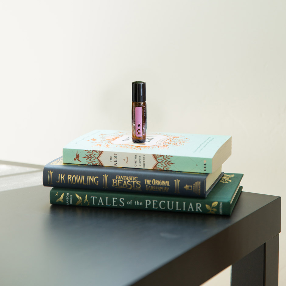 A bottle of InTune Touch essential oils sits on a pile of books on a desk