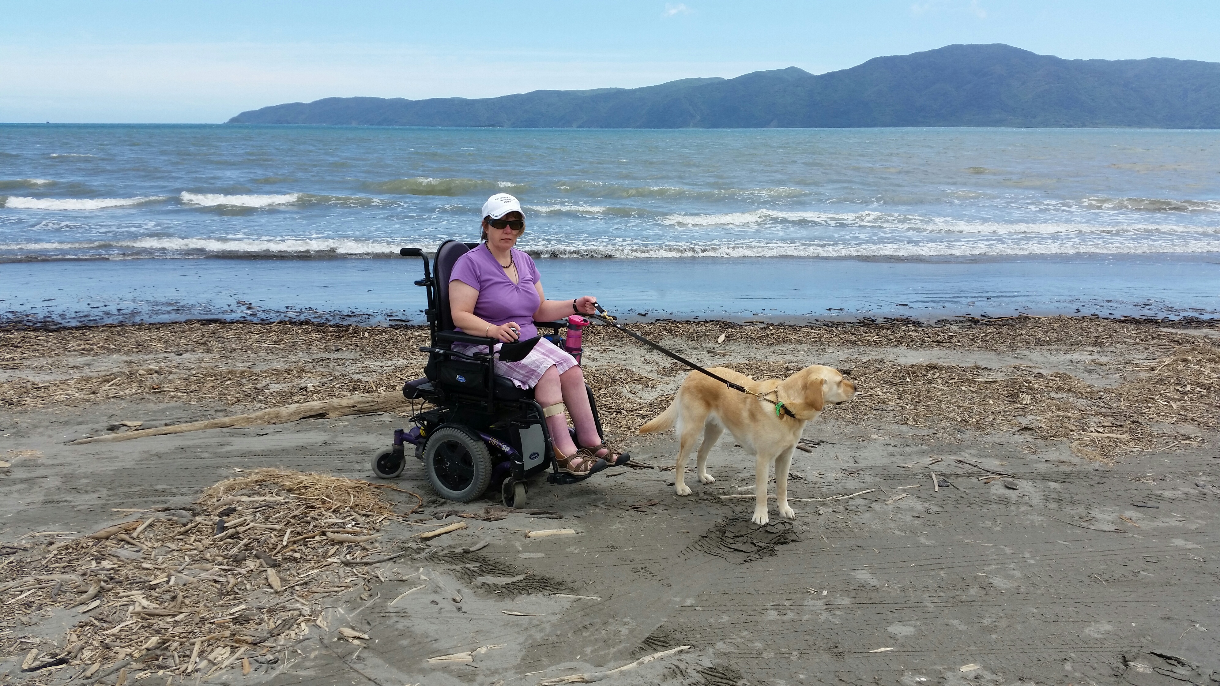 Genevieve in power chair on Kapiti Beach with Guide Dog Pedro