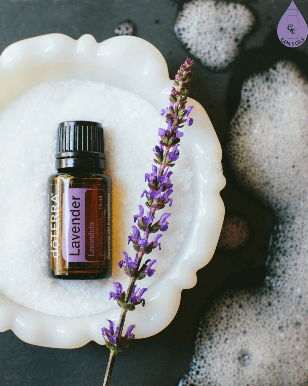 A bottle of doTERRA lavender in a dish of Epsom salts and a sprig of lavender, surrounded by bubbles.