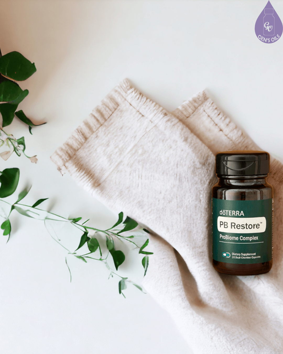 A dark green bottle of doTERRA PB Restore ProBiome Complex dietary supplement sits on a folded light beige cloth next to a potted plant with green leaves.