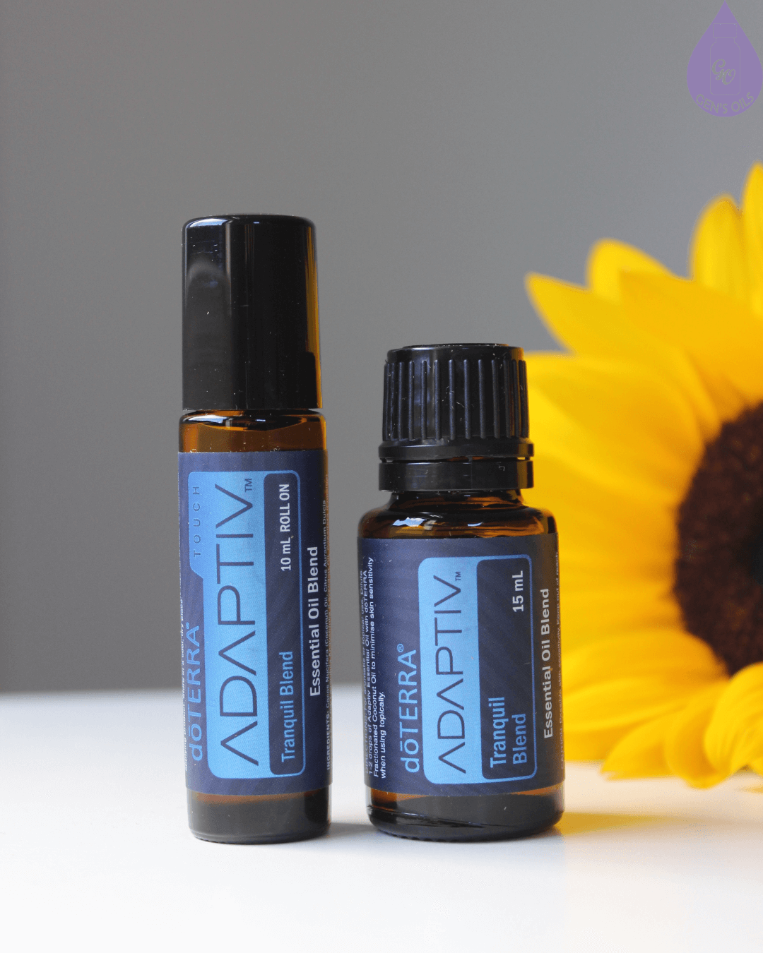 Two bottles of dōTERRA ADAPTIV Tranquil Blend essential oil, one a 10ml roll-on and the other a 15ml bottle, are displayed next to a sunflower.