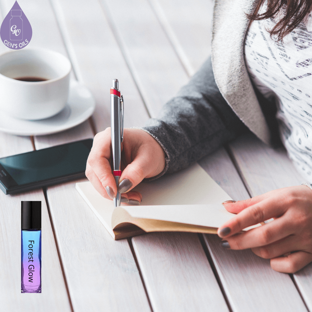 A woman journaling at a table with a cup of tea & a Forest Glow Roller blend.