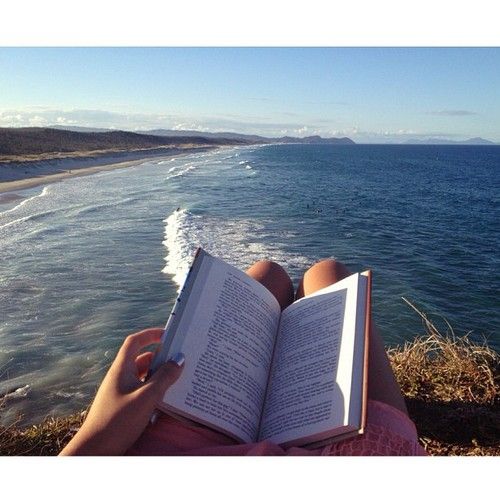 open book propped on lap of woman sitting by the ocean