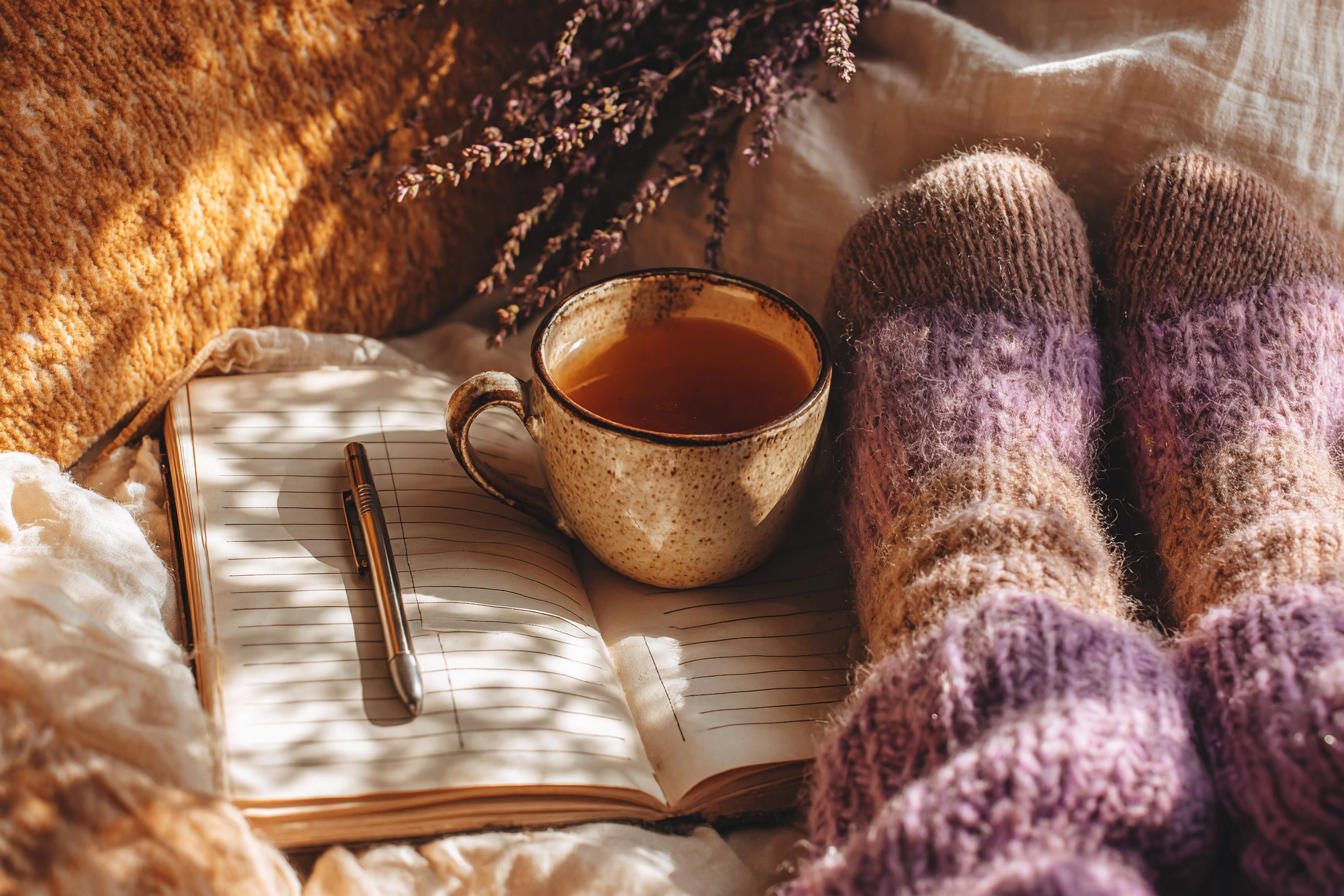 Bare feet in soft purple wool socks beside a mug of herbal tea, open journal and dried lavender, a quiet moment of rest during the two week wait