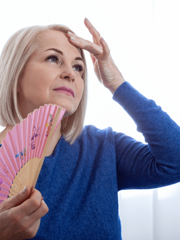 Middle-aged woman experiencing hot flush from menopause using a fan for relief
