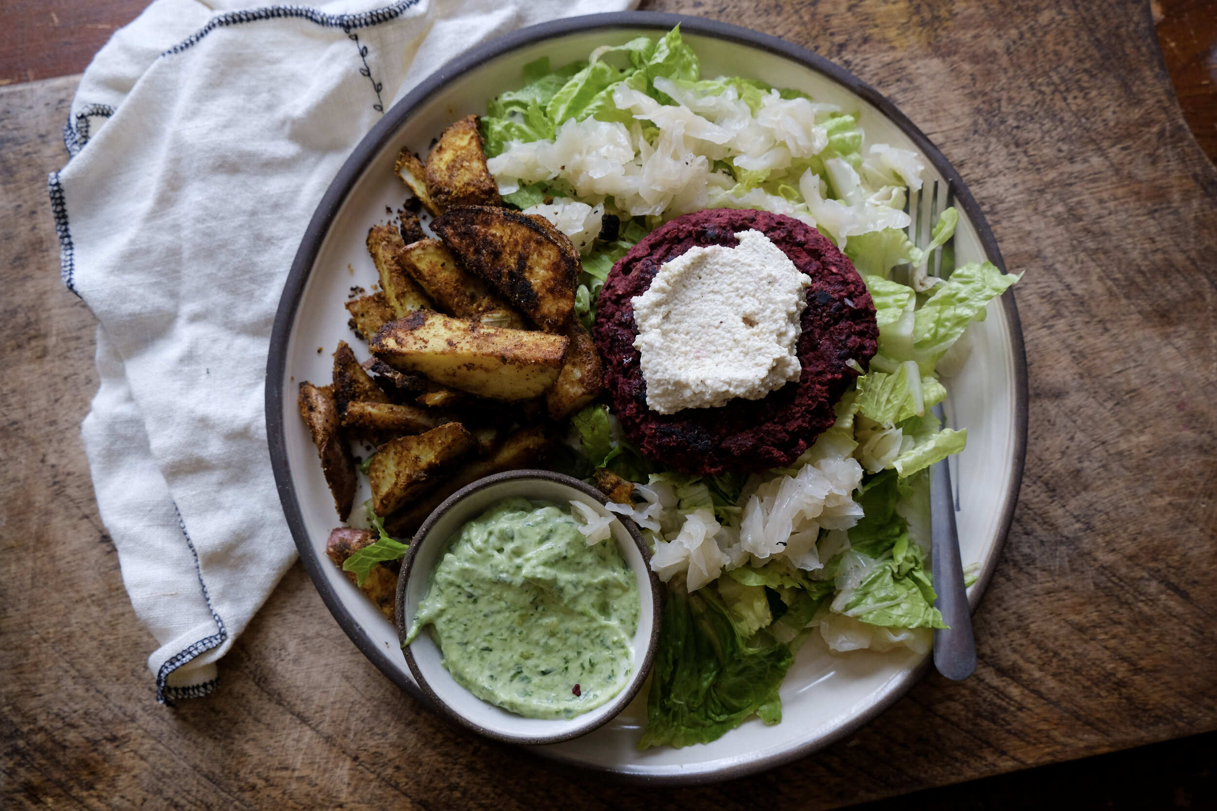A simple (if some things are meal prepped in advance) throw together salad with romaine lettuce, kraut, beet burger topped with  cashew chèvre , homefries, and creamy pesto “mayo”